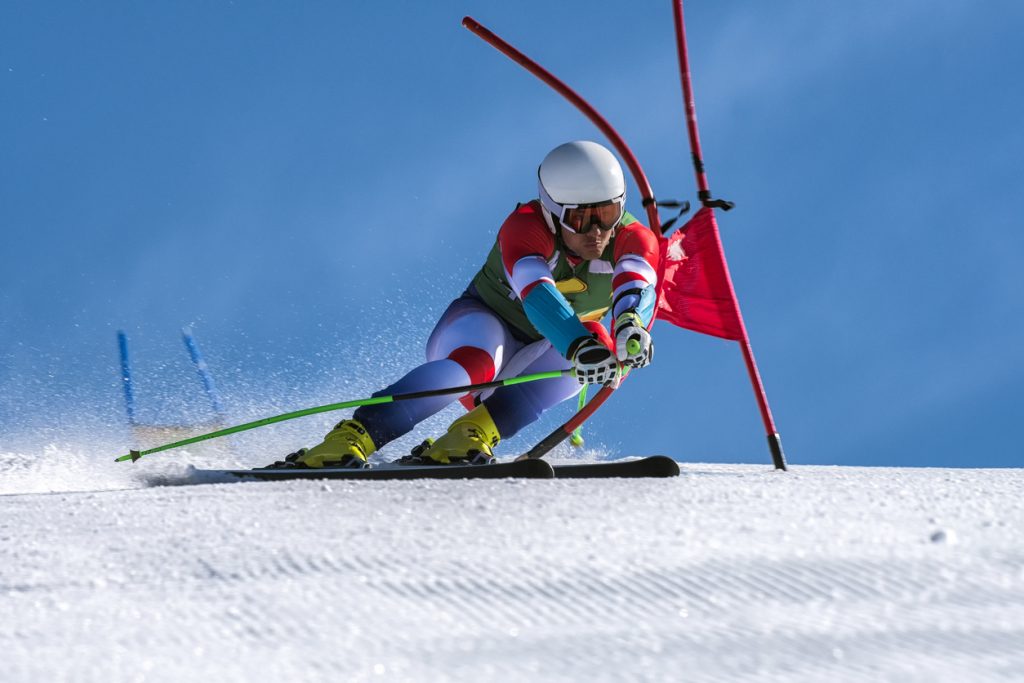 Young man compeeting at giant slalom race, bending the red gate, against the blue sky