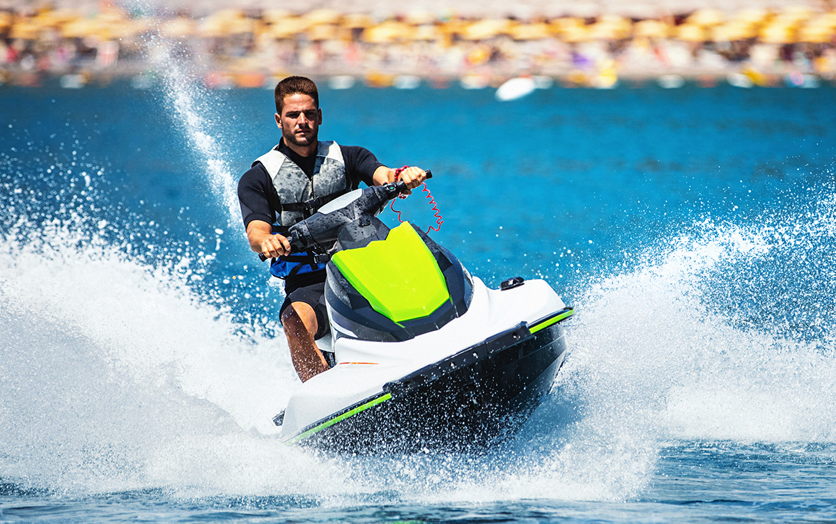 Closeup front view of a young man riding a jet ski on a sunny summer day at open sea. He's wearing swimming suit and a life jacket.